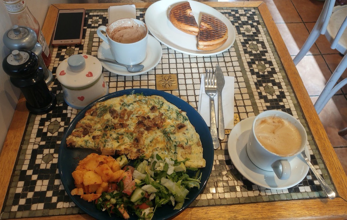 A mushroom and spinach omelette with potatoes and salad, a toasted cheese panini, hot chocolate and a coffee on the mosaic-tiled table at Camia Delicatessen