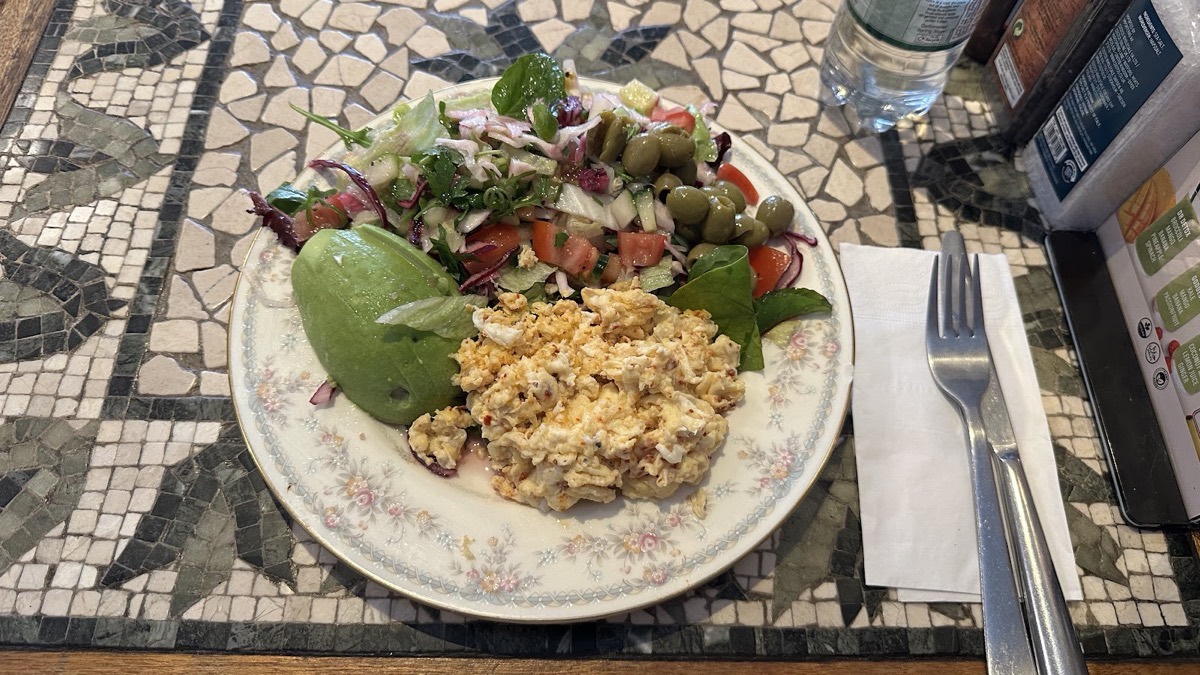 Scrambled eggs served with a fresh green salad and olives on a vintage plate at Camia Delicatessen, Stoke Newington