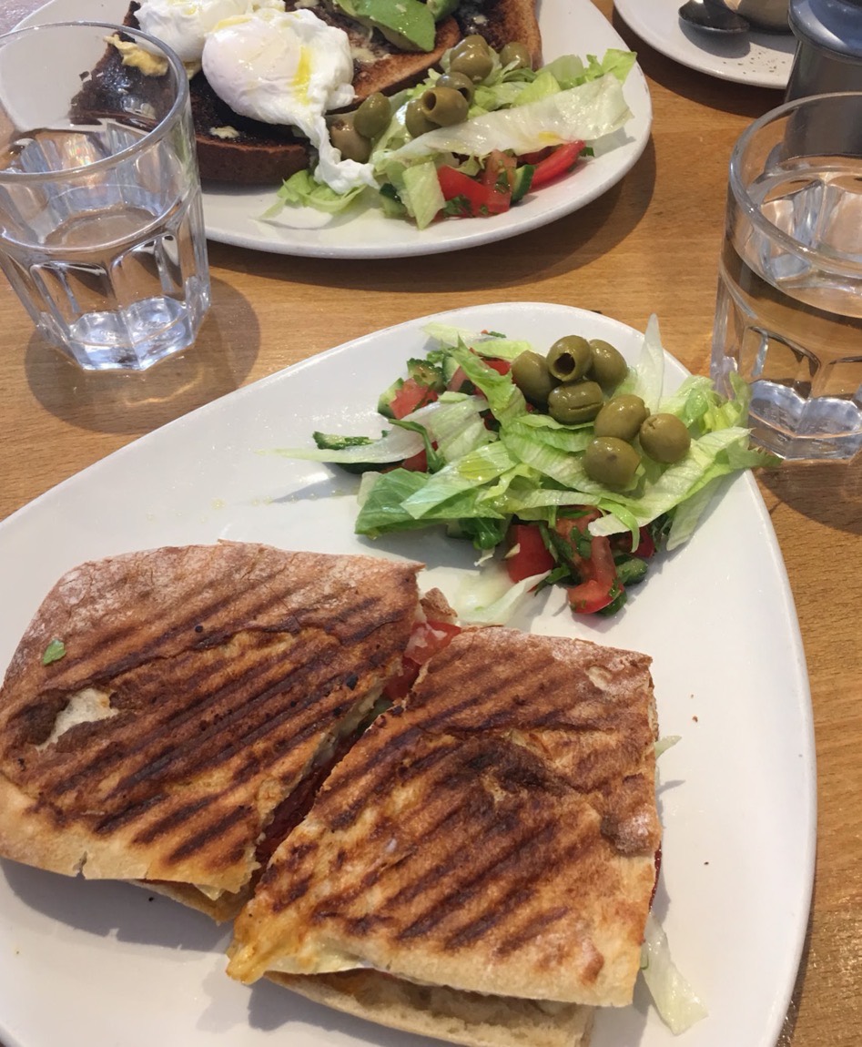 A toasted panini and poached eggs on toast with a fresh side salad and olives, served at Camia Delicatessen in Stoke Newington